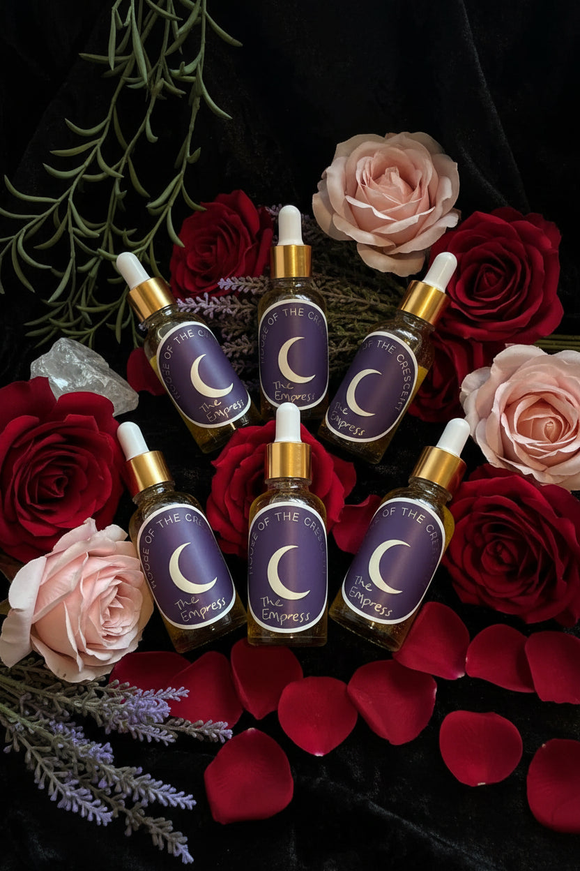 A bottle and tube of 'The Empress' ritual oil arranged on a dark velvet surface with dried lavender, a crystal, and greenery.