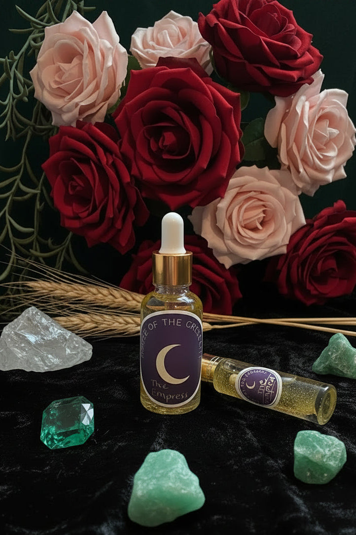 A bottle and tube of 'The Empress' ritual  oil by House of the Crescent arranged on a dark velvet surface with dried lavender, a crystal, and greenery.