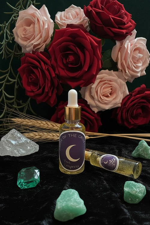 A bottle and tube of 'The Empress' ritual  oil by House of the Crescent arranged on a dark velvet surface with dried lavender, a crystal, and greenery.